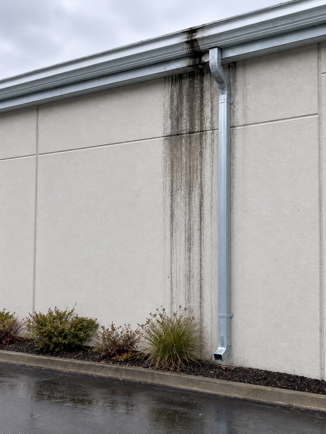 Dark water staining below a damaged gutter and downspout connection