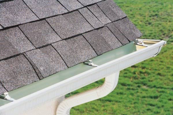 White gutter and downspout secured along an asphalt-shingle roof