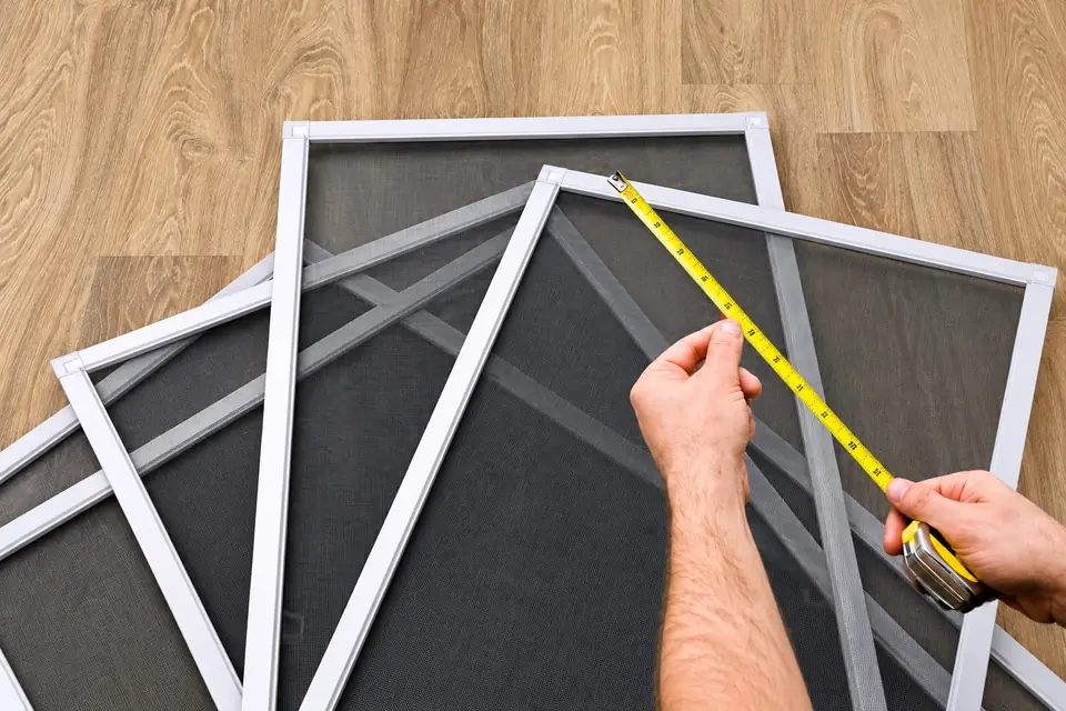 Hands using a yellow tape measure across a white custom window screen frame