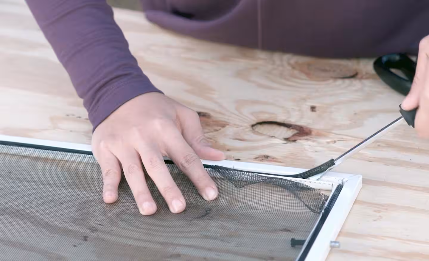 Hands replacing damaged mesh in a window screen frame