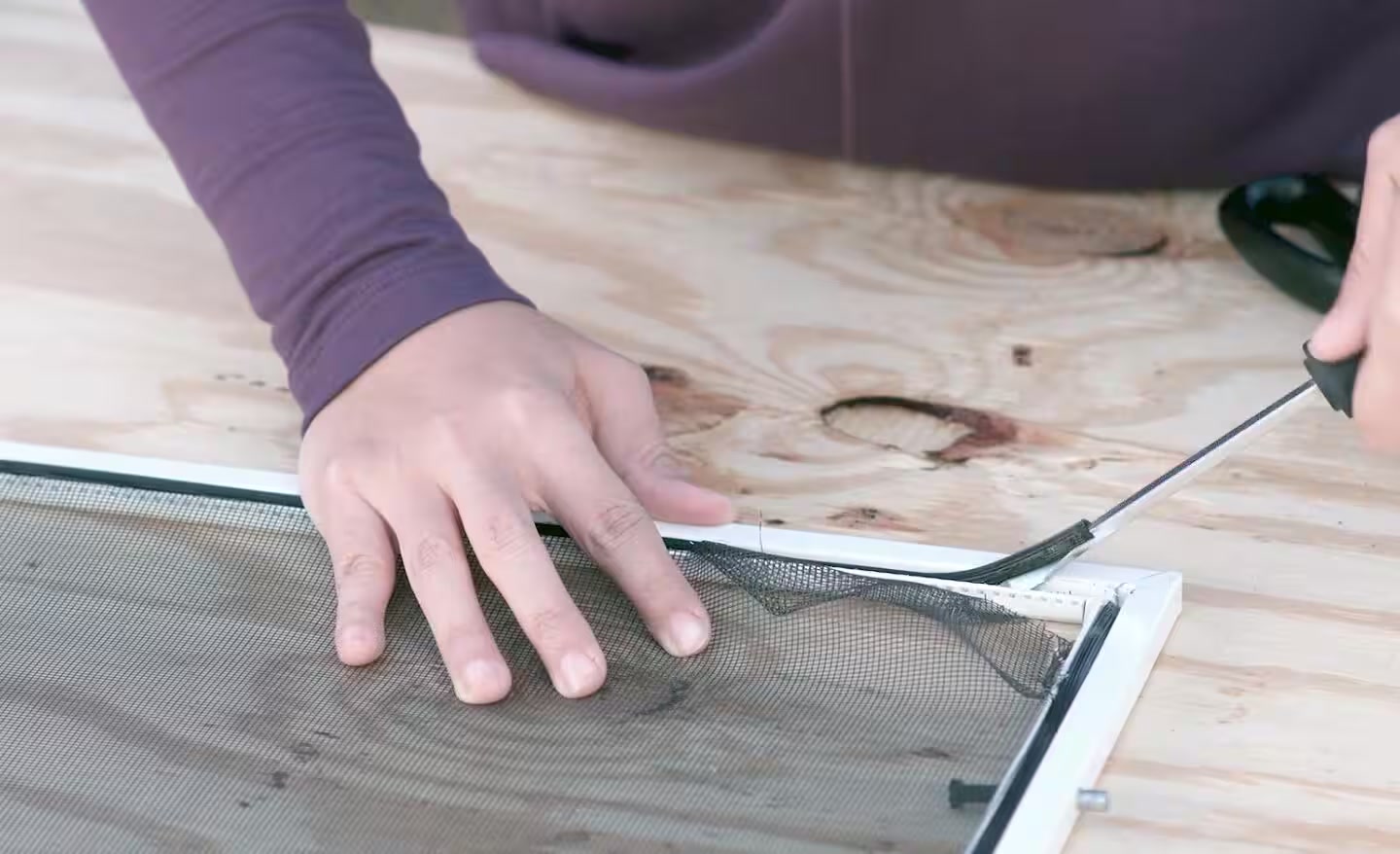 Hands replacing damaged mesh in a window screen frame