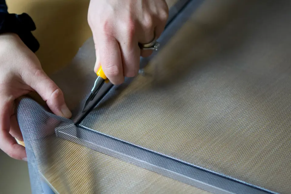 Hands installing new mesh into a window screen frame with a spline roller